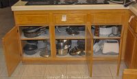 Kitchen cabinets open showing various stacked pots, pans, and lids arranged inside lower cabinets.