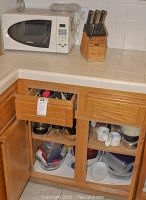 White microwave oven with keypad on countertop next to wooden knife block with knives in it. Under counter cabinets open showing plastic storage containers inside.