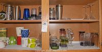 Shelf with assorted mugs in various colors and designs on bottom shelf, jars and glassware on top shelf