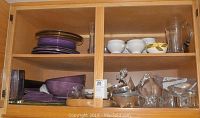 Image showing various serving dishes arranged on wooden shelves including purple ceramic plates and bowls, pewter appetizer bowls, and French onion soup bowls along with clear glassware.