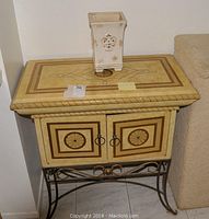 Front view of ornate decorative serving table with inlaid top, double door storage below, and metal base with scrollwork.