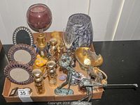Photo showing the collection of vanity items including perfume bottles, picture frames, and glass vases inside a cardboard tray on a black surface