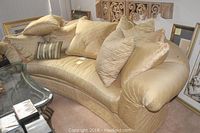 Front angled view of curved gold silk sofa with multiple down-filled pillows, showing overall shape and condition.