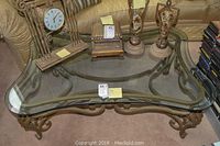 Full view of metal scrollwork base and curved glass top with decorative items