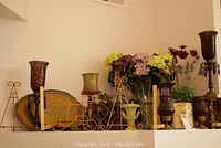 View of decorative items including purple and brown candle holders, ceramic vases, metal stands, and artificial flowers on shelf.