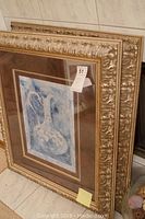 Two framed wall art pieces stacked against the wall, showing ornate gold-colored frames with vase artwork.