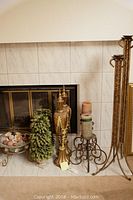 Wide view of decorative items against tile fireplace including candleholders, floral arrangement, urn, decorative bowl with balls, and framed art.