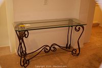 Front view of glass top console table with decorative iron base showing scroll details.