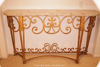 Front view of marble top table showing decorative metal base with scroll details and rectangular cream marble surface.