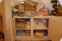 Full view of white shelf with cabinet doors opened showing folded sheets, linens, and duvets stacked inside and on top.
