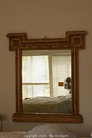 Front view of mirror hanging on wall reflecting window and bed