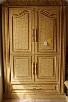 Front view of beige crackled finish freestanding armoire with paneled doors and vertical handles.