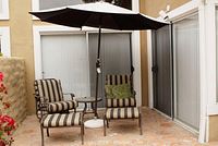 Wide-angle photo of the patio set showing 2 club chairs, table, and umbrella in an outdoor patio corner.