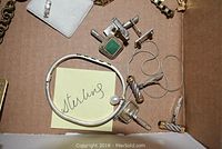 Top view of assorted silver cufflinks, bracelets, and a pearl sterling bracelet with post-it note 'sterling'