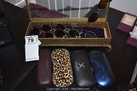 Gilt and glass vanity box holding six pairs of assorted eyeglasses and sunglasses, four eyeglass cases nearby.