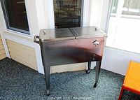 Front view of rectangular stainless steel cooler with two lids and bottle opener attached on the side.