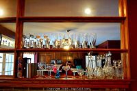Wide view of assorted glassware on two shelves, includes pilsner glasses with logos, stemware, and cut glass decanters