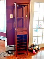 Front view of the tall wood and laminate wine rack showing drawer, bottle compartments, shelves, and stemware rack.