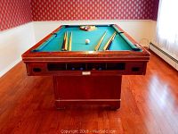 Front view of Valley Manufacturing Co pool table on wood floor with 6 cues laid across it, showing wood frame condition.