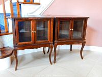 Pair of wooden side tables with glass door fronts and cabriole legs, shown together from the front.