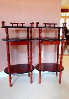 Pair of three-level wooden side tables with turned legs, each with a drawer and decorative railing on the top shelf, showing wear.