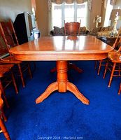 Full view of oak dining table with four curved legs and rounded edges, surrounded by six matching oak chairs on blue carpet.