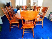 Eight oak finish wooden dining chairs arranged around a dining table showing backs and seats