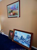 Three pieces of wall art against beige wall and blue carpet. Two leaning on wall, one hanging, showing frames and overall size.