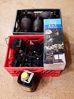 Overview of crate containing multiple black Tiki lamps and boxed Tiki 4-in-1 torch.