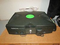 Angle showing front of original Xbox console with green Xbox logo and controller ports.