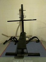 Front view of Soloflex exercise machine showing bench and pull-up bar attachment on black steel frame.
