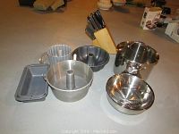 Photo showing baking pans (Bundt, bread, angel food cake), colander, stock pot, mixing bowl, and wooden knife block with knives in background.