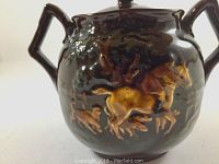 Side view of dark brown glazed sugar bowl with raised hunting scene featuring horse and dogs.
