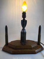 WWII trench art lamp showing the front with lamp lit, wooden octagonal base, two shell casings on each side, and central shell casing lamp body.