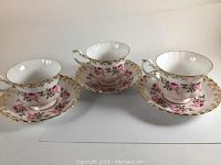 Three tea cups with matching saucers arranged in a row, showing floral and gold designs.