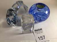 Four glass art paperweights with differing shapes and designs placed on a white surface with lot label