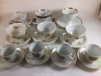 Overview of all ten cups and saucers, showing various designs, floral and fruit patterns, and gold trim