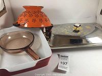 Overview photo showing all four items: lasagna pan, saute pan, orange colander, and silver serving dish with lid