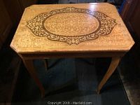 Music box table top showing rectangular shape, curved legs and intricate inlay design in varying wood tones forming a central oval medallion pattern