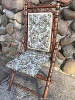 Front view of Victorian folding chair set against stone wall, displaying floral tapestry seat and backrest, turned wooden frame details.