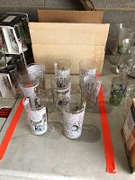 Set of eight clear drinking glasses displayed in original cardboard box; each glass features printed black and white political cartoon graphics and text bubbles by J.R. Williams.