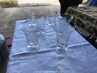 Six clear crystal glasses arranged on a white tablecloth showing the shape and design of each glass.