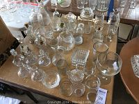 Table covered with various clear glassware including decanters, jars, small bowls, plates, and drinking glasses.