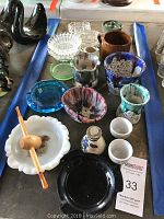 Top down photo showing an assortment of 18 pottery bowls, ashtrays, a pipe, and ceramic pieces on a blue table runner.