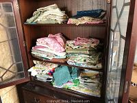 Wooden cabinet with three shelves holding folded towels, sheets, and fabric linens