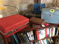 Overview of red Forecast suitcase and two brown grooming kits placed on bookshelf.