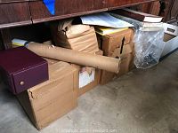 Six cardboard boxes and some additional containers underneath a wooden desk, partially wrapped and sealed, presumably containing National Geographic magazines and other materials as indicated by seller description.