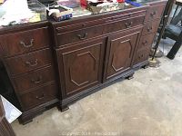 Front view of wooden sideboard with paneled doors and drawers, brass hardware handles visible.