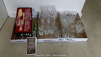 Overview of all set items displayed on the floor showing glassware, cutlery, and serving pieces in three cardboard trays