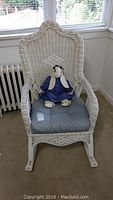 Full front view of white wicker rocking chair with cushion and bunny doll seated